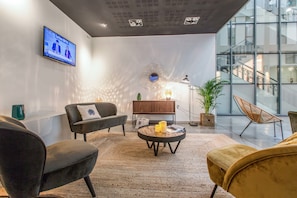 A modern living room with a sofa, armchair, and round coffee table. A television is mounted on the wall, and there is a staircase visible in the background. - Appart'City Classic Lyon Part-Dieu (Lyon)