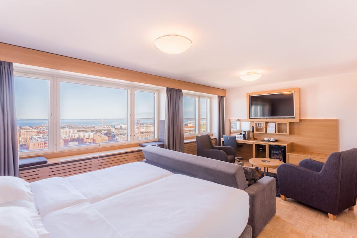 Une chambre d’hôtel avec un grand lit, un canapé, une télévision et une vue sur la ville.