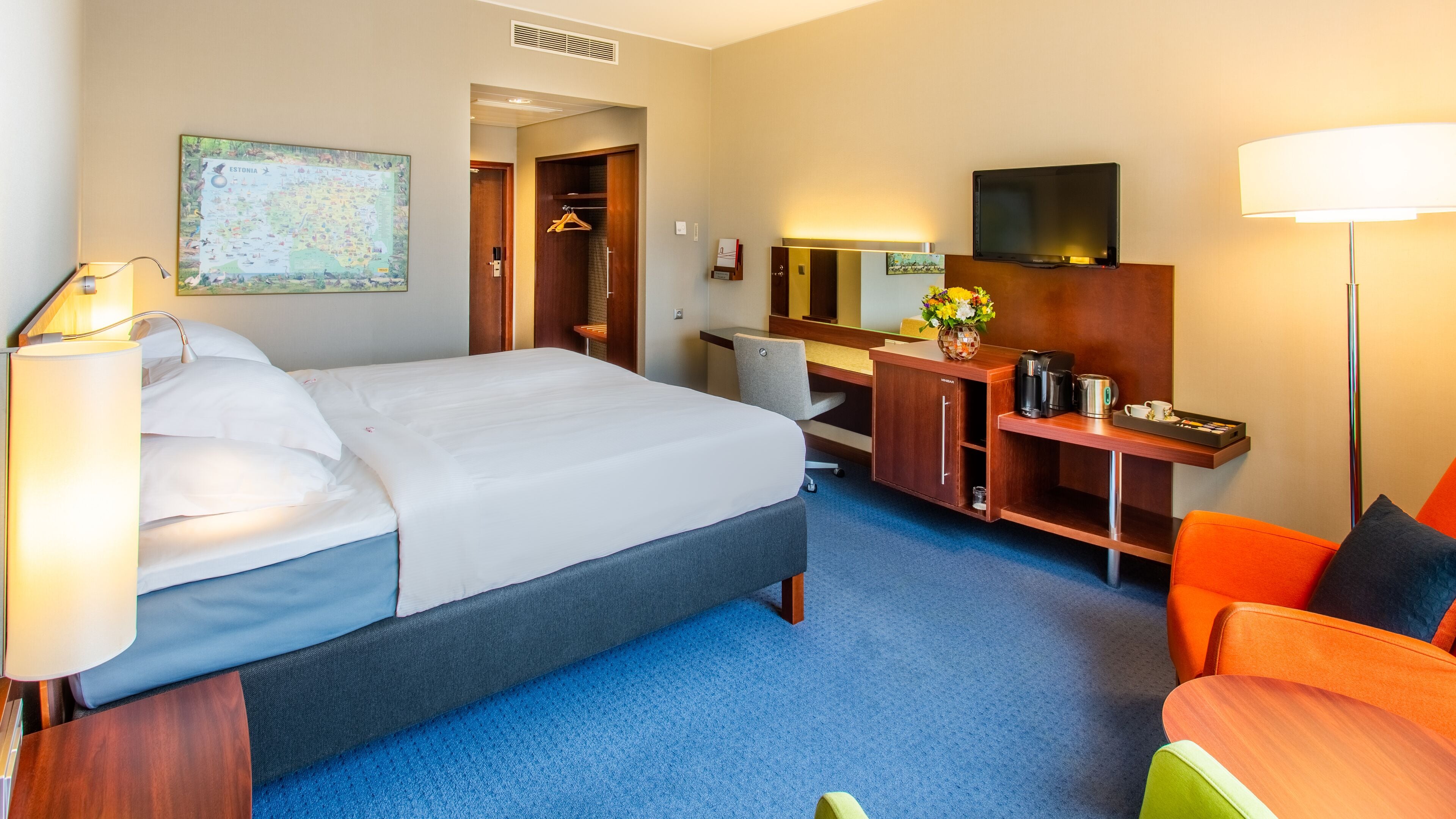A hotel room with a bed, desk, chair, TV, and a map on the wall.