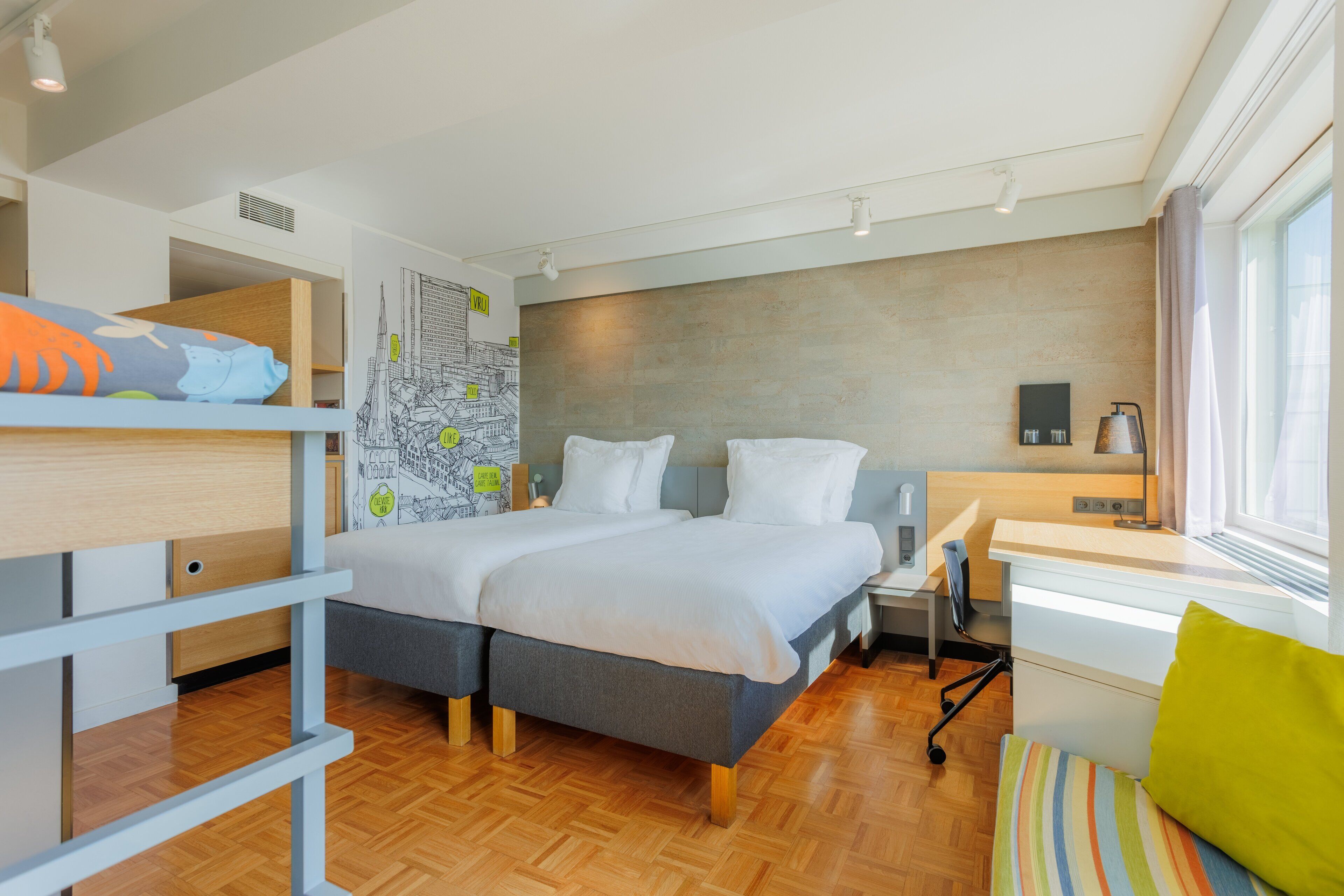A modern hotel room with a large bed, a desk, and a window with curtains.