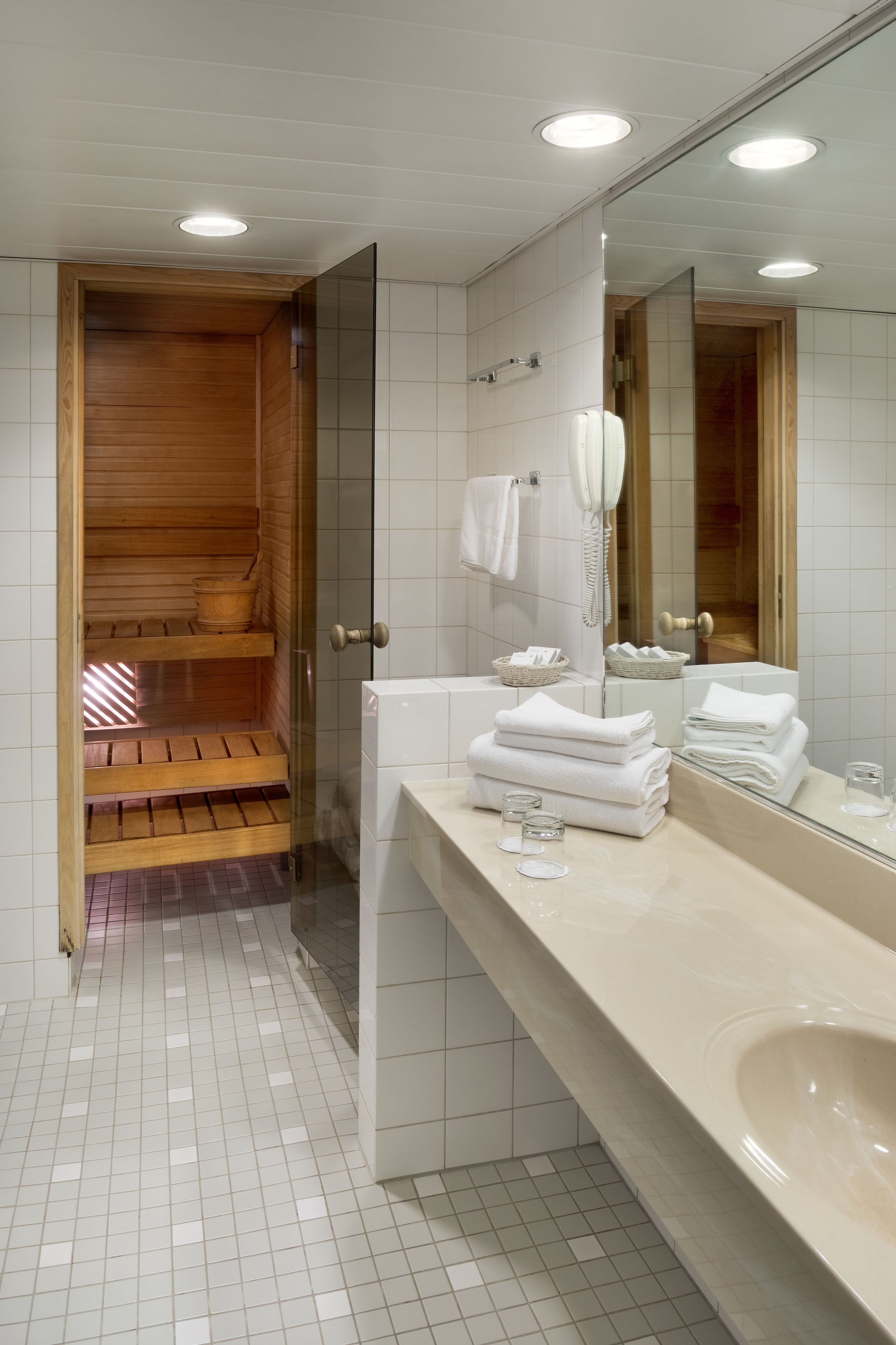 Une salle de bain moderne avec un sauna en bois, un grand miroir et des serviettes soigneusement pliées.