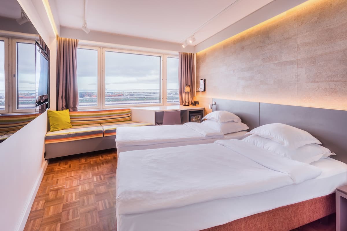 Une chambre d’hôtel avec deux lits, une fenêtre donnant sur un beau paysage, un bureau et une lampe.