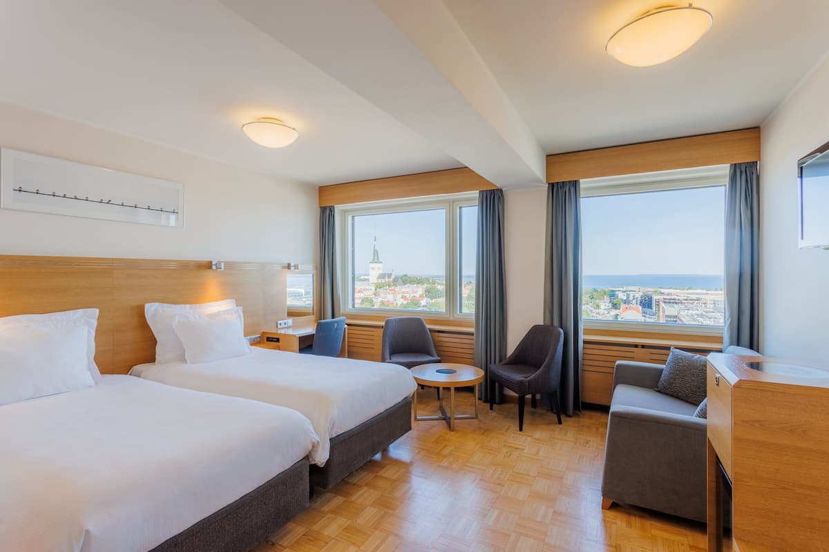 Une chambre d’hôtel avec deux lits, un bureau, une chaise et une vue sur la ville.