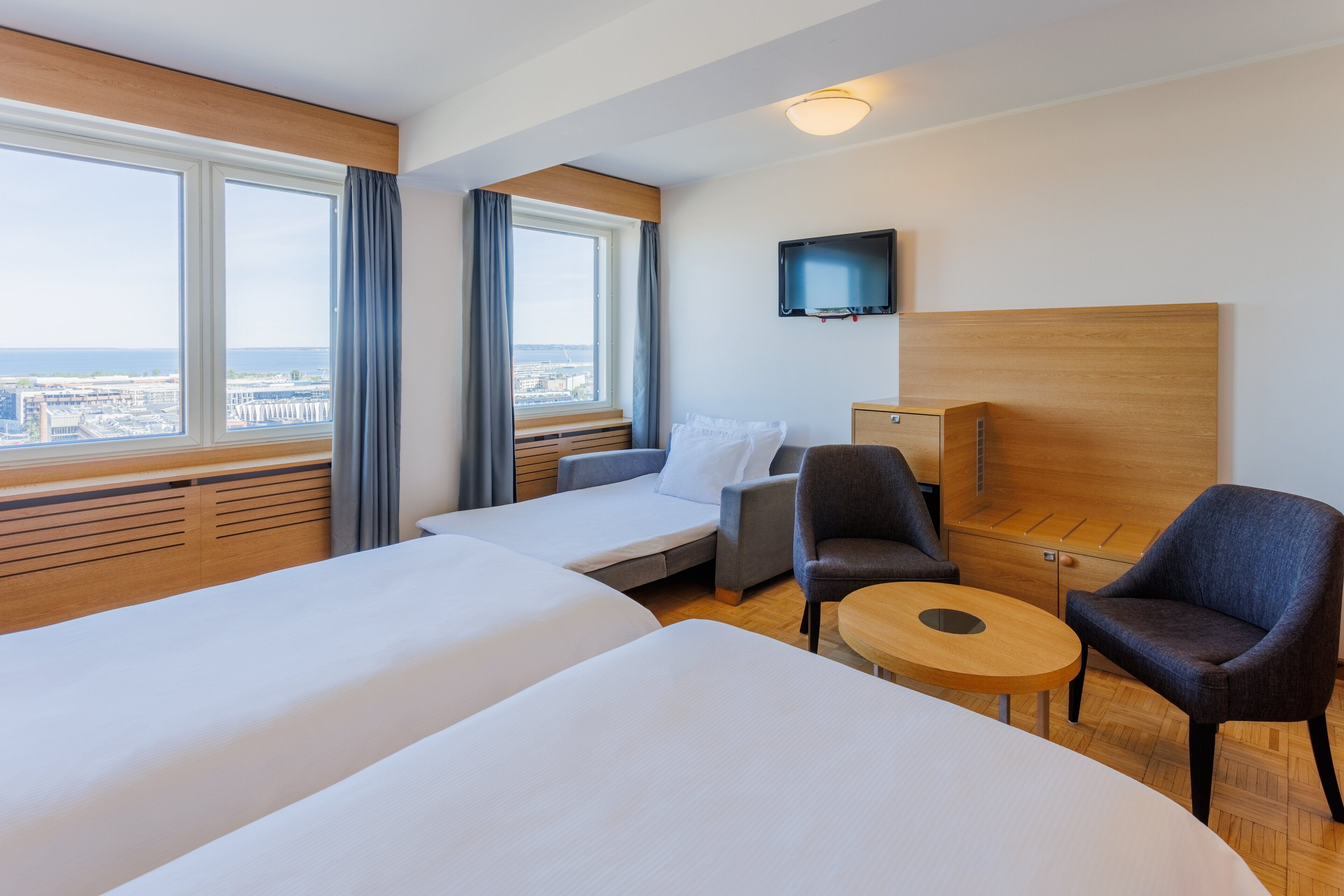 A hotel room with two beds, a TV, a desk, and a view of the city.