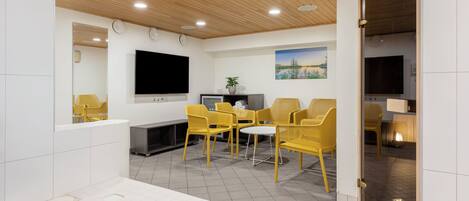 A modern indoor pool area with a wooden ceiling, a flat-screen TV, and yellow chairs.