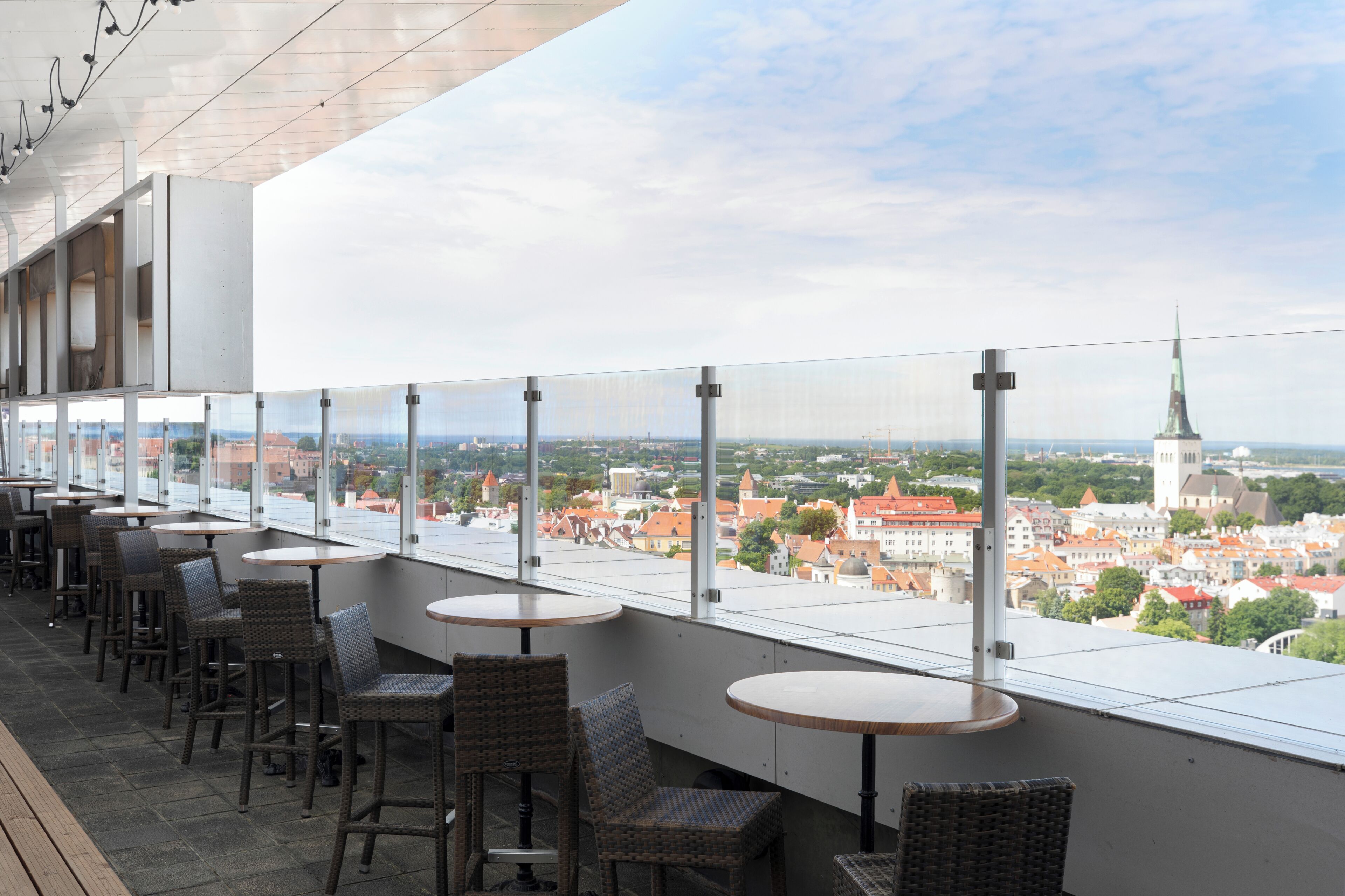 Una terraza con mesas y sillas, con vistas a un paisaje urbano con edificios y una torre.
