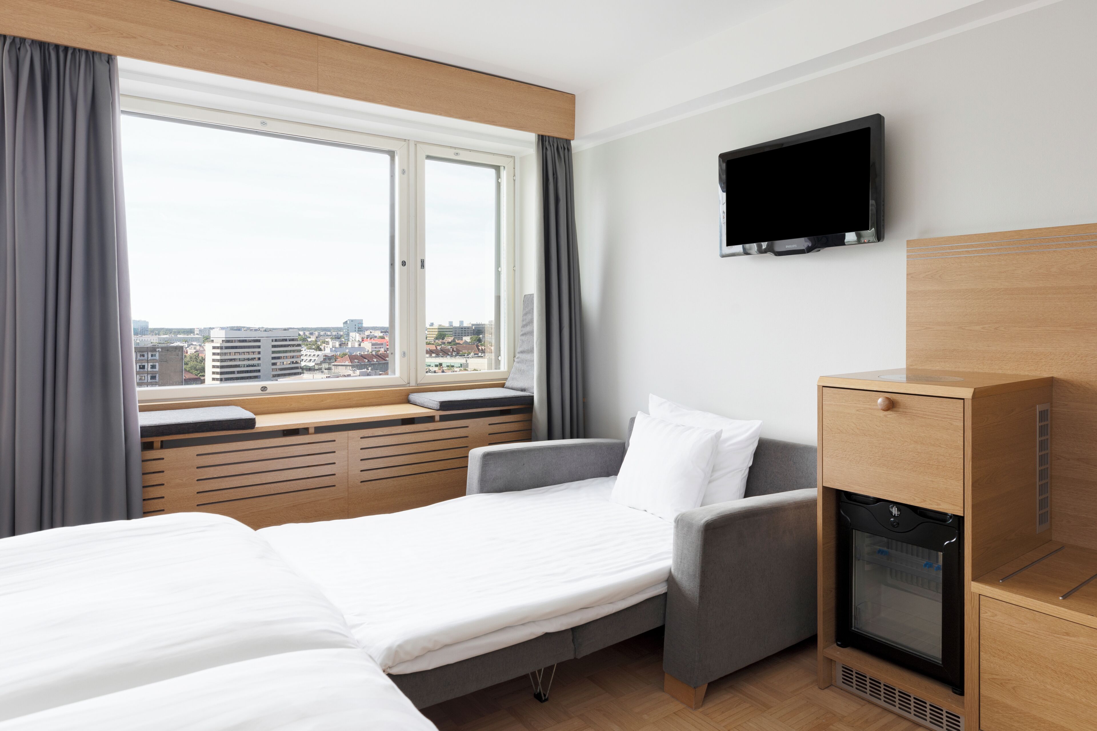 A hotel room with two beds, a television, a minibar, and a window with curtains.