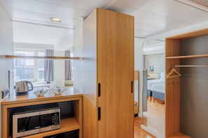 Een moderne hotelkamer met een houten garderobe, een magnetron, een waterkoker en een bed met uitzicht op de stad.