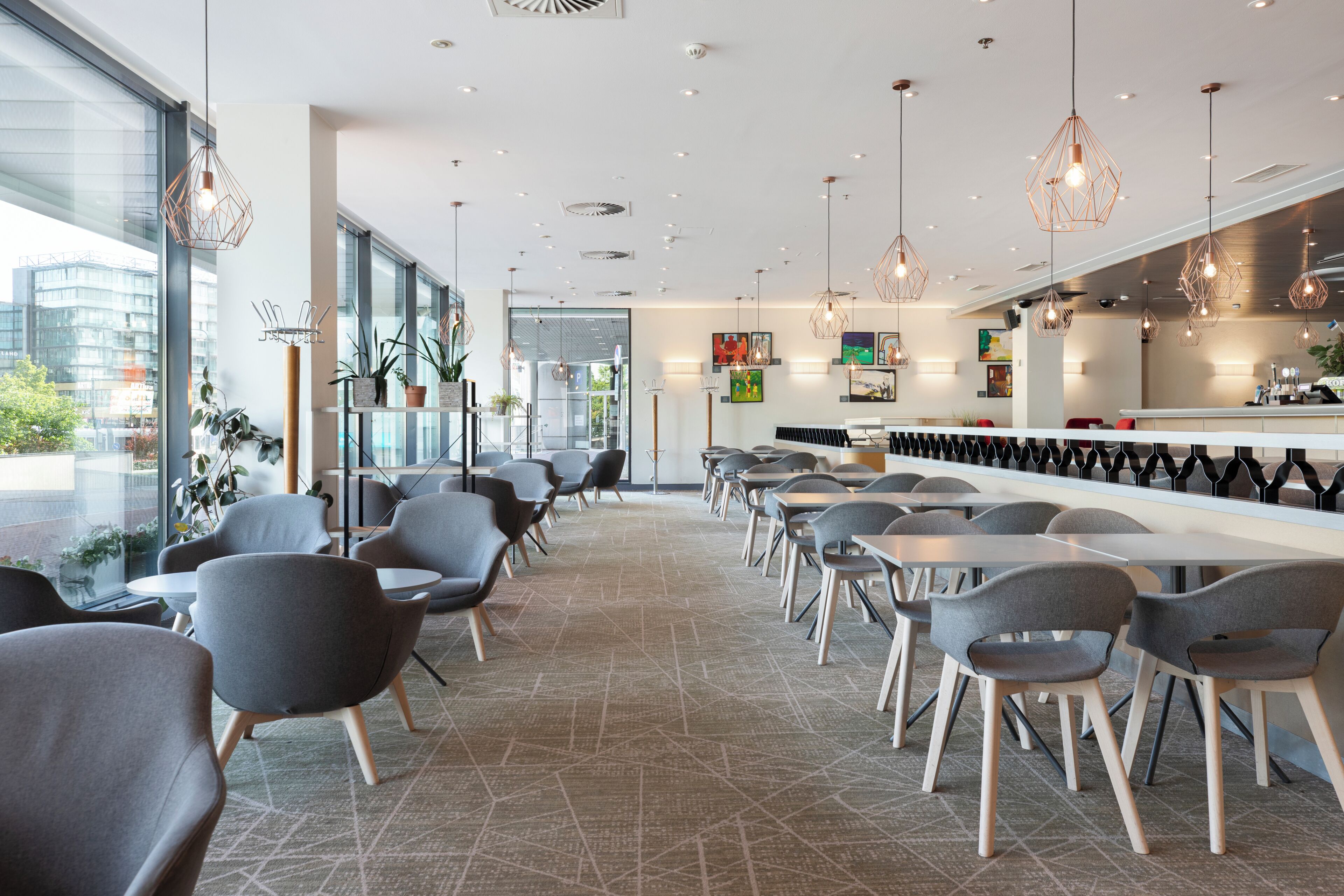 Ein modernes Café mit einer langen Theke, mehreren Sitzbereichen und Pendelleuchten.
