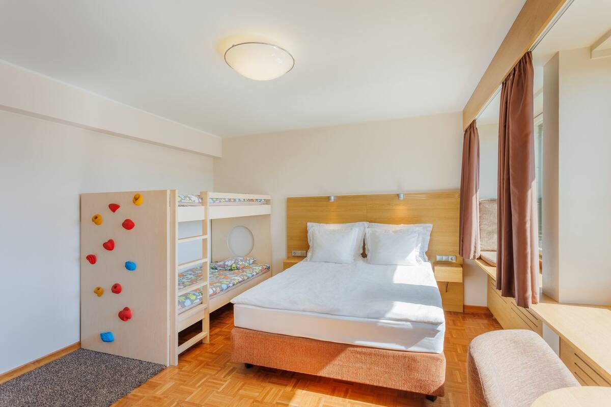 Une chambre d’hôtel moderne équipée d’un lit superposé, d’un mur d’escalade et d’une grande fenêtre avec des rideaux.