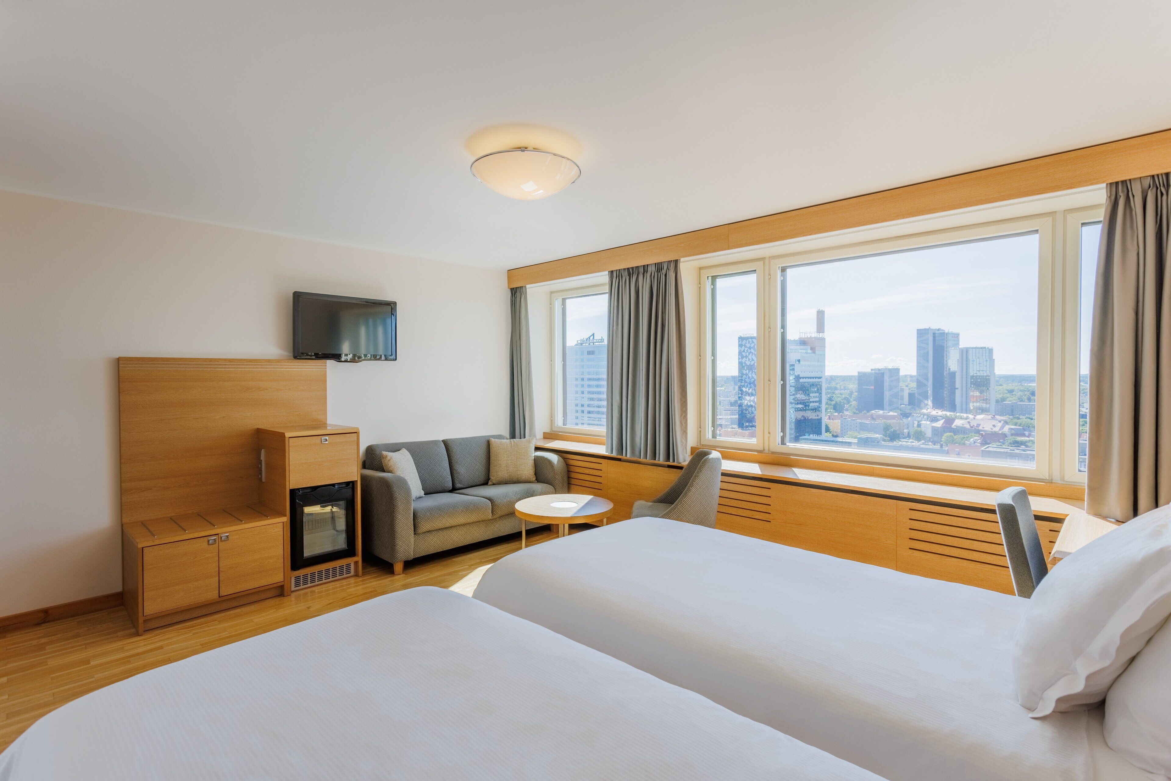 A hotel room with two beds, a sofa, a TV, and a city view.