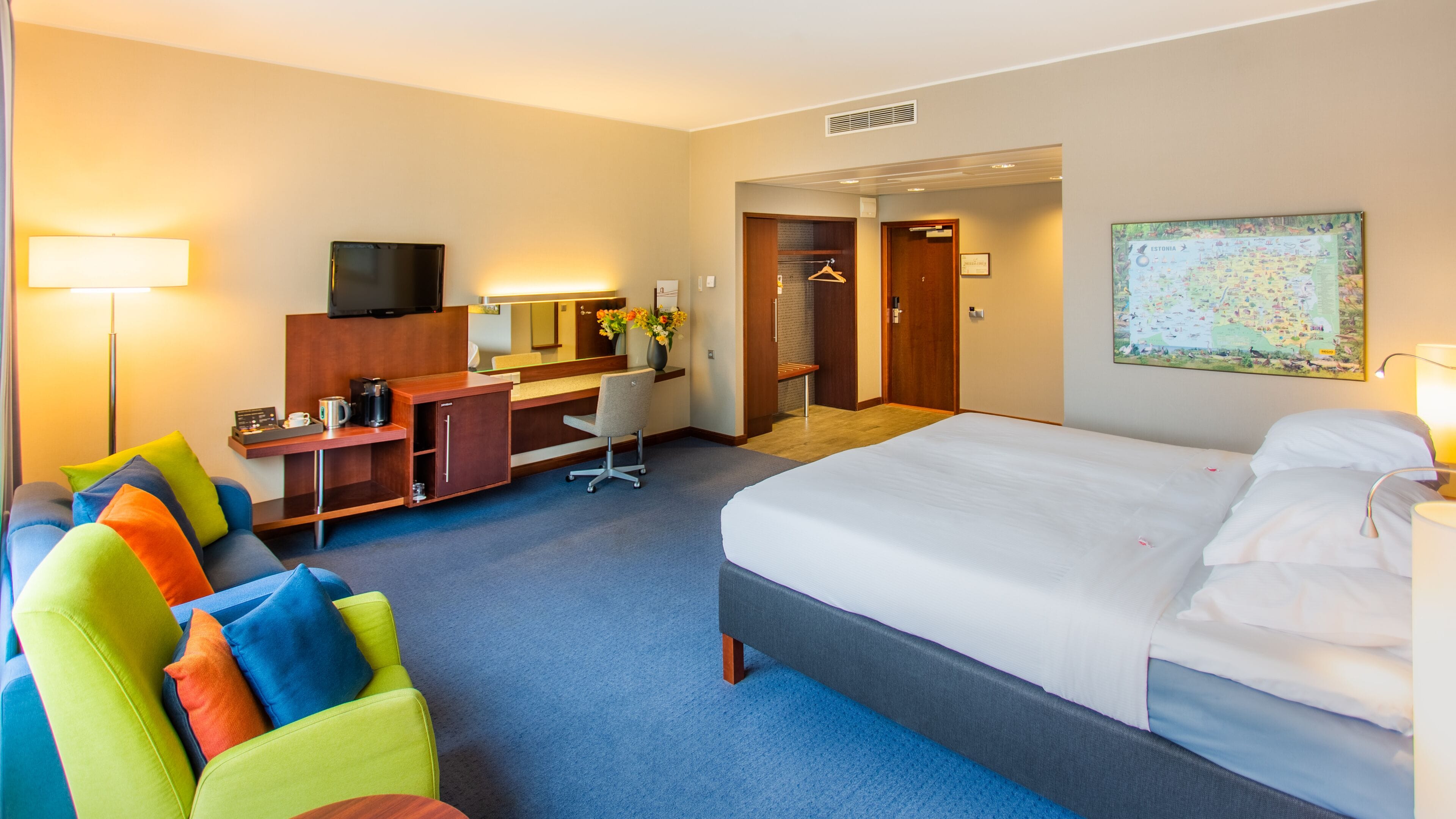Habitación de hotel con cama, escritorio, silla, televisor y un mapa en la pared.
