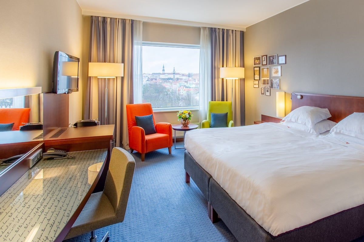 Une chambre d’hôtel avec un grand lit, un bureau, deux chaises, une télévision et une fenêtre donnant sur la ville.