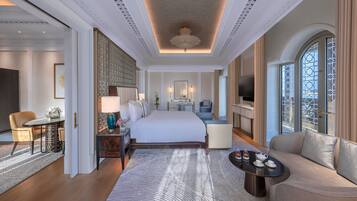 Quarto de hotel espaçoso com uma cama grande, área de estar com sofá, mesa de jantar e televisão.
