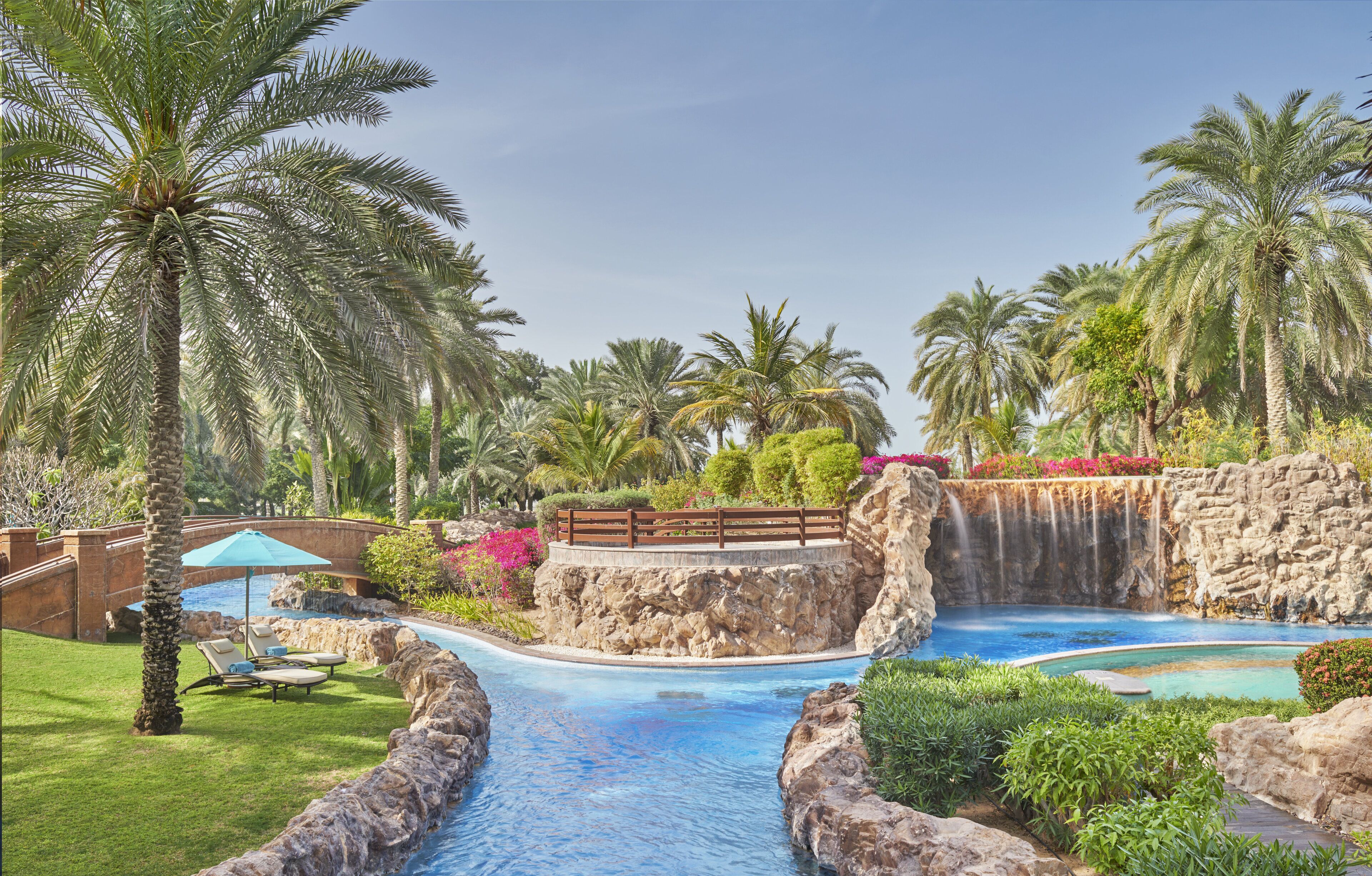 A resort pool area with palm trees, a waterfall, and a bridge.
