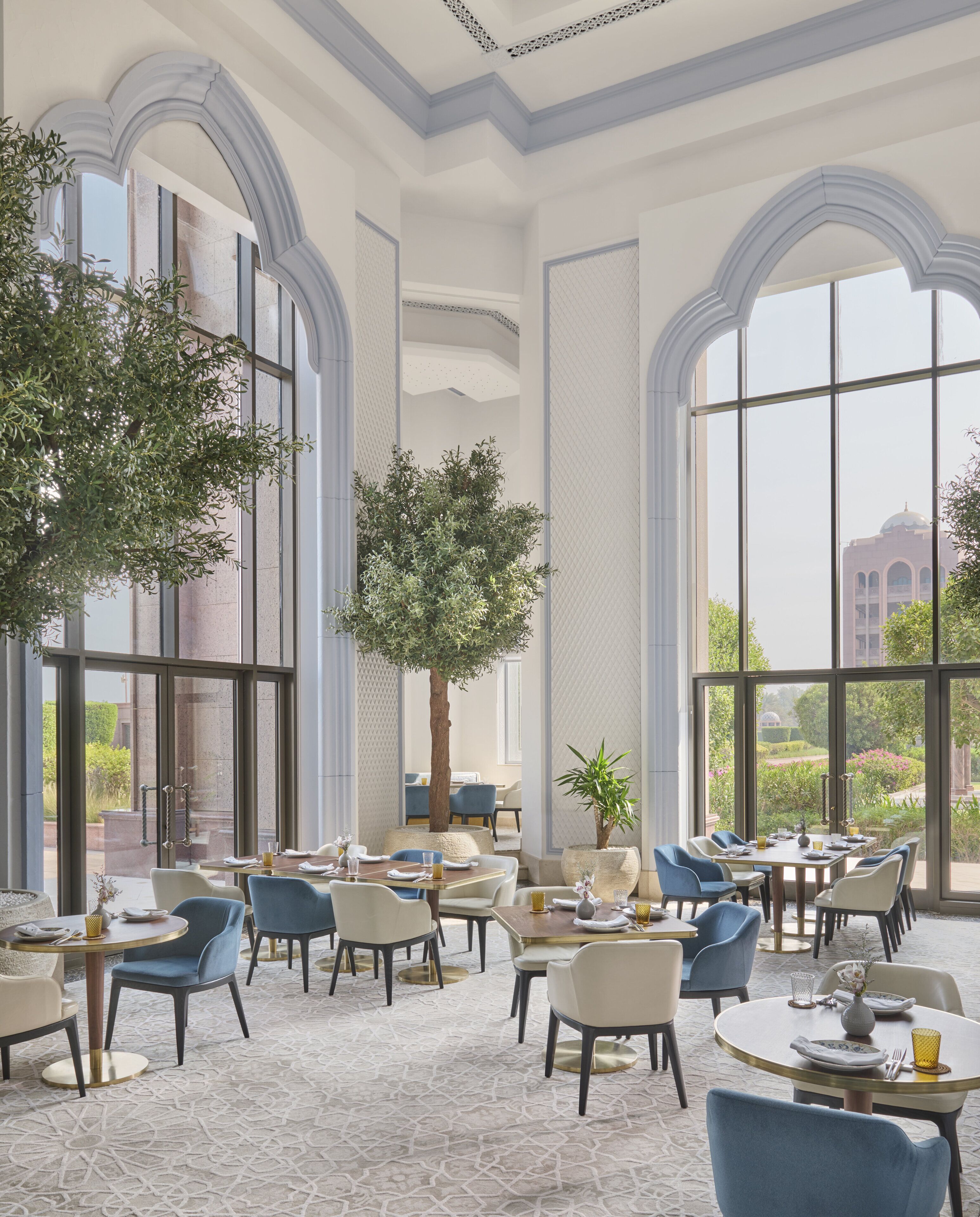A spacious dining area with high ceilings and large windows, featuring modern furniture and a view of the surrounding landscape.