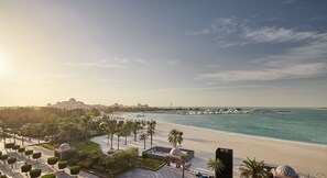 A coastal resort with a beachfront promenade, palm trees, and a view of the sea and distant buildings.