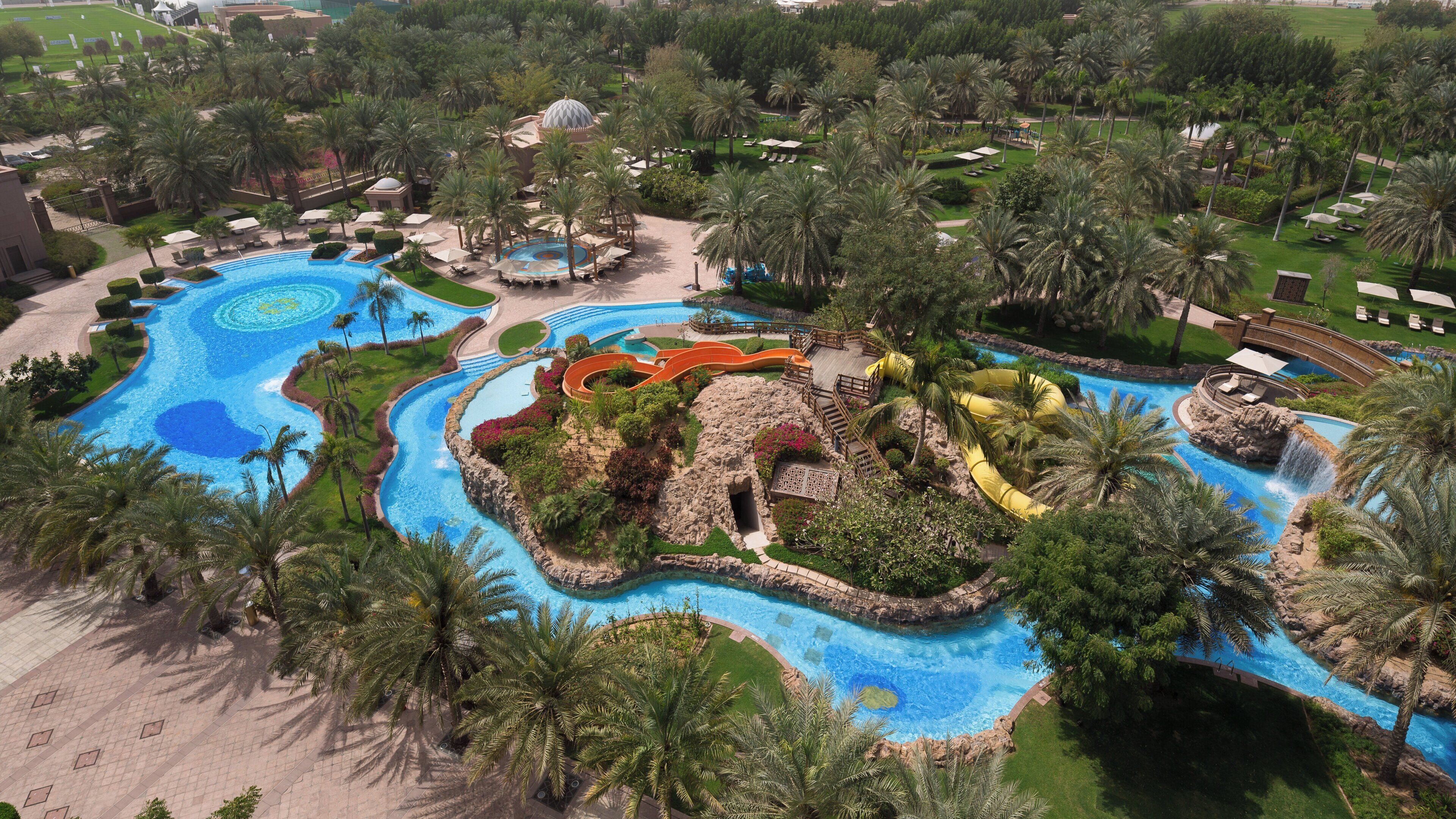 Un complexe hôtelier doté de plusieurs piscines, de palmiers et d’une cascade artificielle.