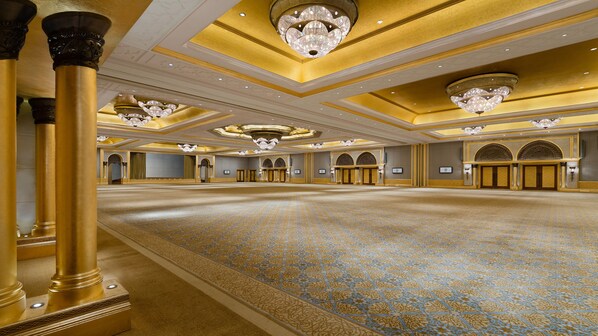 Un vaste hall agrémenté de lustres somptueux, de colonnes dorées et d’un tapis à motifs.