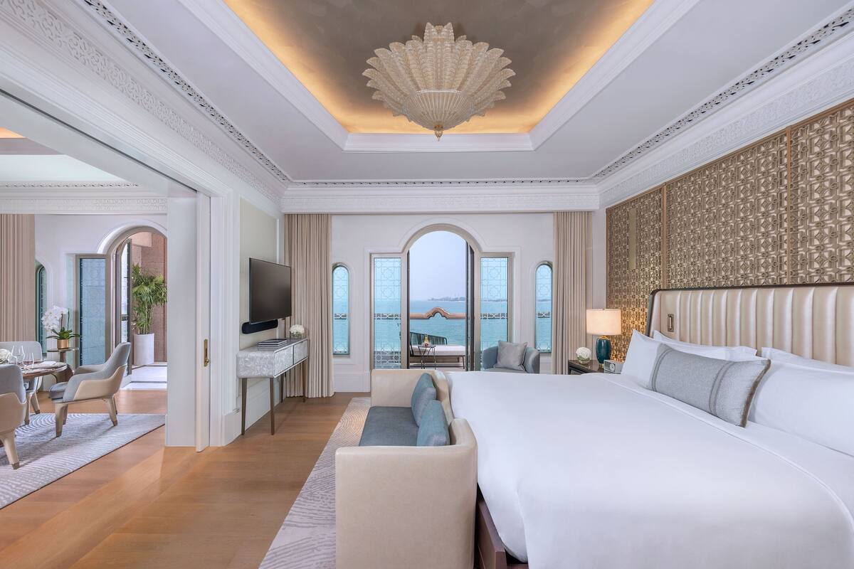 A luxurious hotel room with a large bed, a TV, a seating area, and a view of the sea.