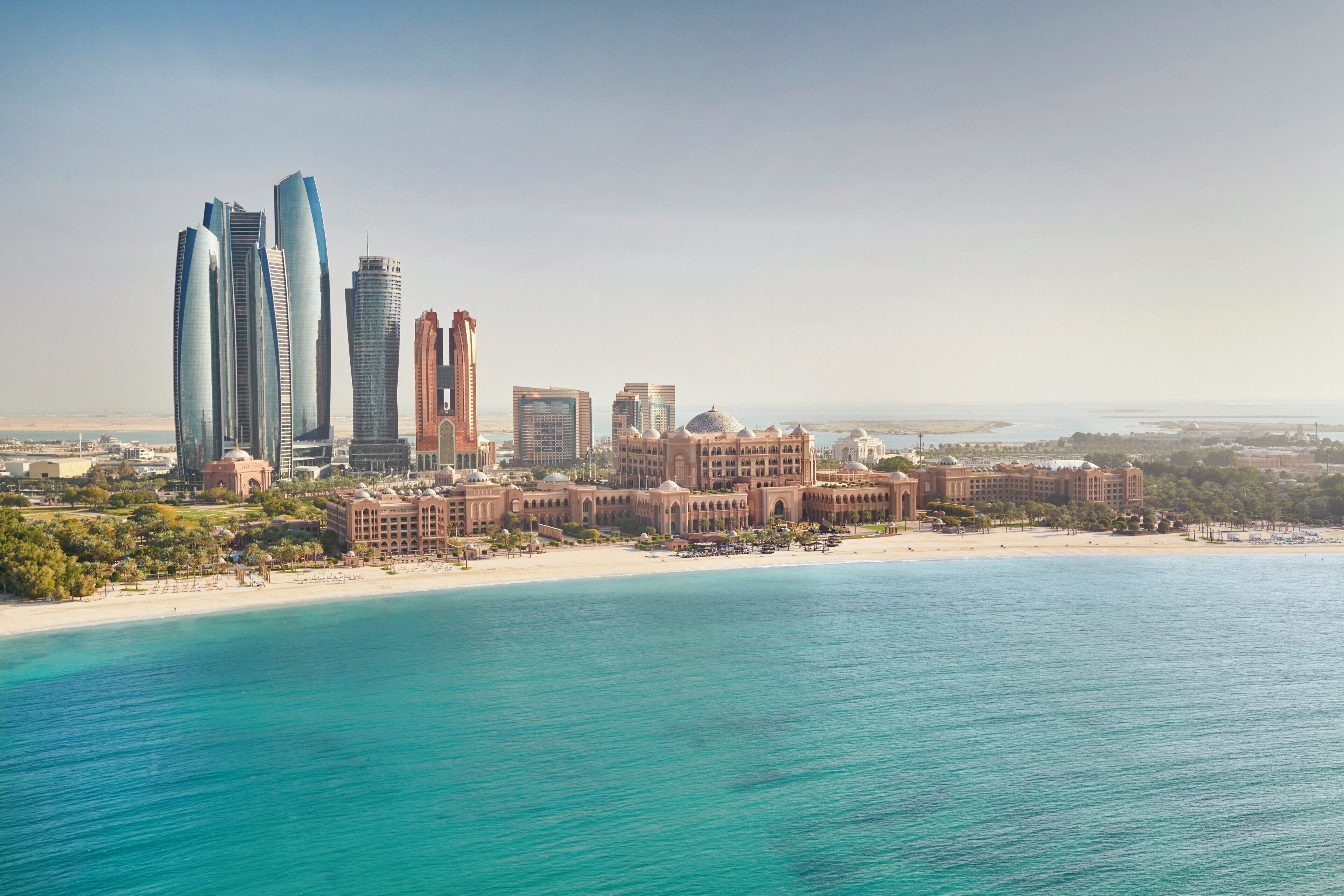 A coastal cityscape with modern skyscrapers, a beach, and a large hotel with domed architecture.