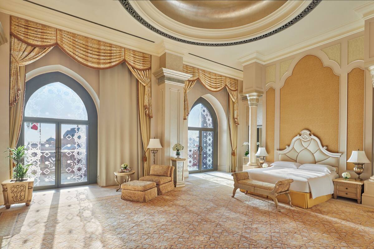 A luxurious bedroom with a large bed, ornate curtains, and a view through a large arched window.