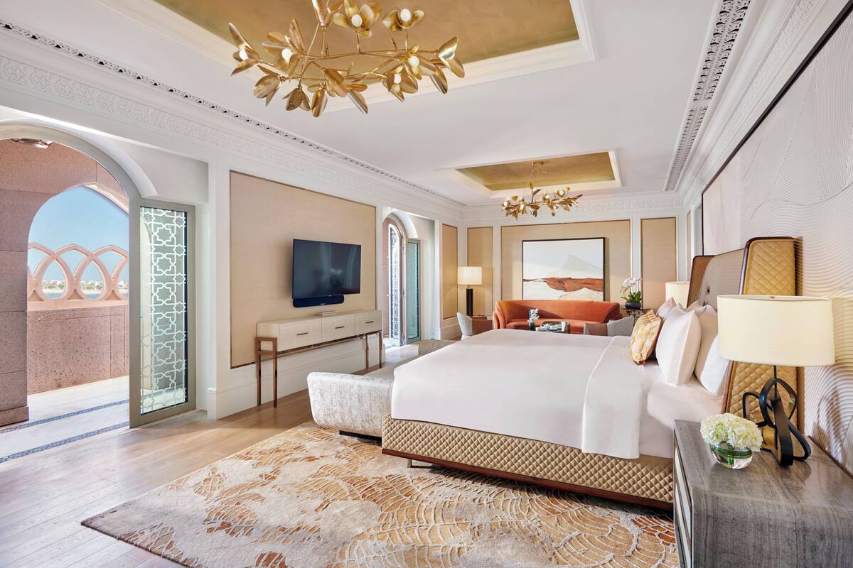 A spacious bedroom with a large bed, a television, a desk, and a view of the outdoors.