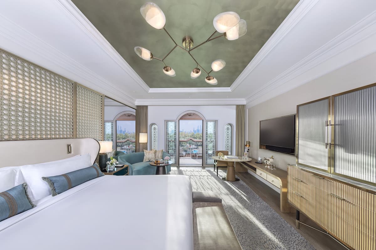 Ein geräumiges Hotelzimmer mit einem großen Bett, einer Sitzecke mit Tisch und Stühlen, einem Fernseher und einem Balkon mit Blick auf die Stadt.