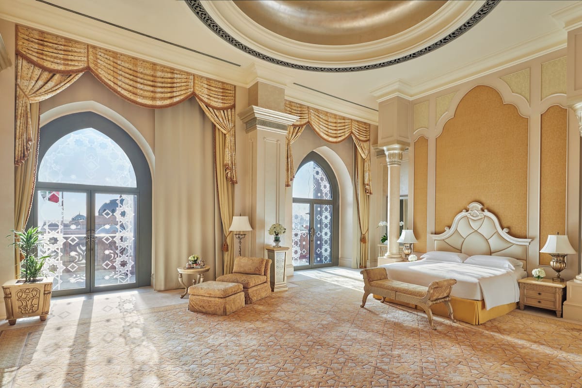 Ein luxuriöses Schlafzimmer mit einem großen Bett, aufwendigen Vorhängen und Blick durch ein großes, rundes Fenster.