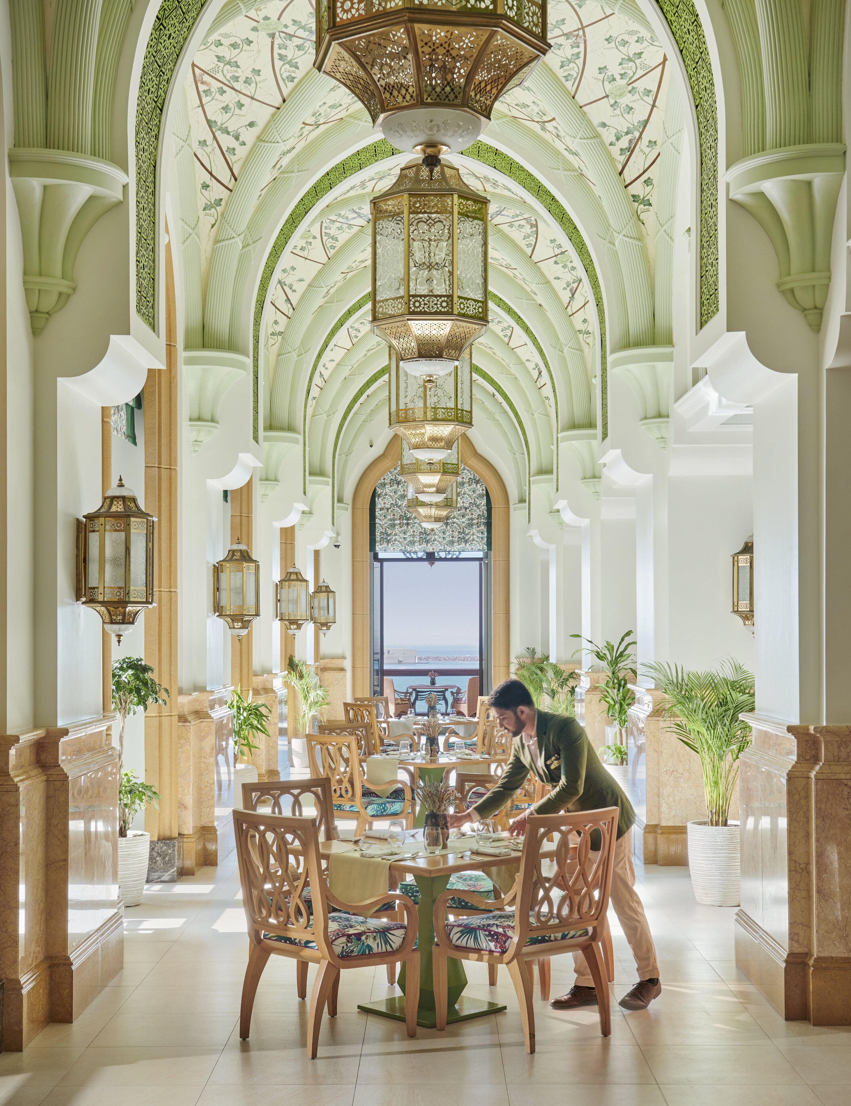 A spacious lobby with high arched ceilings, ornate chandeliers, and a view of the sea through large windows.