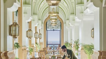 A spacious lobby with high arched ceilings, ornate chandeliers, and a view of the sea through large windows.
