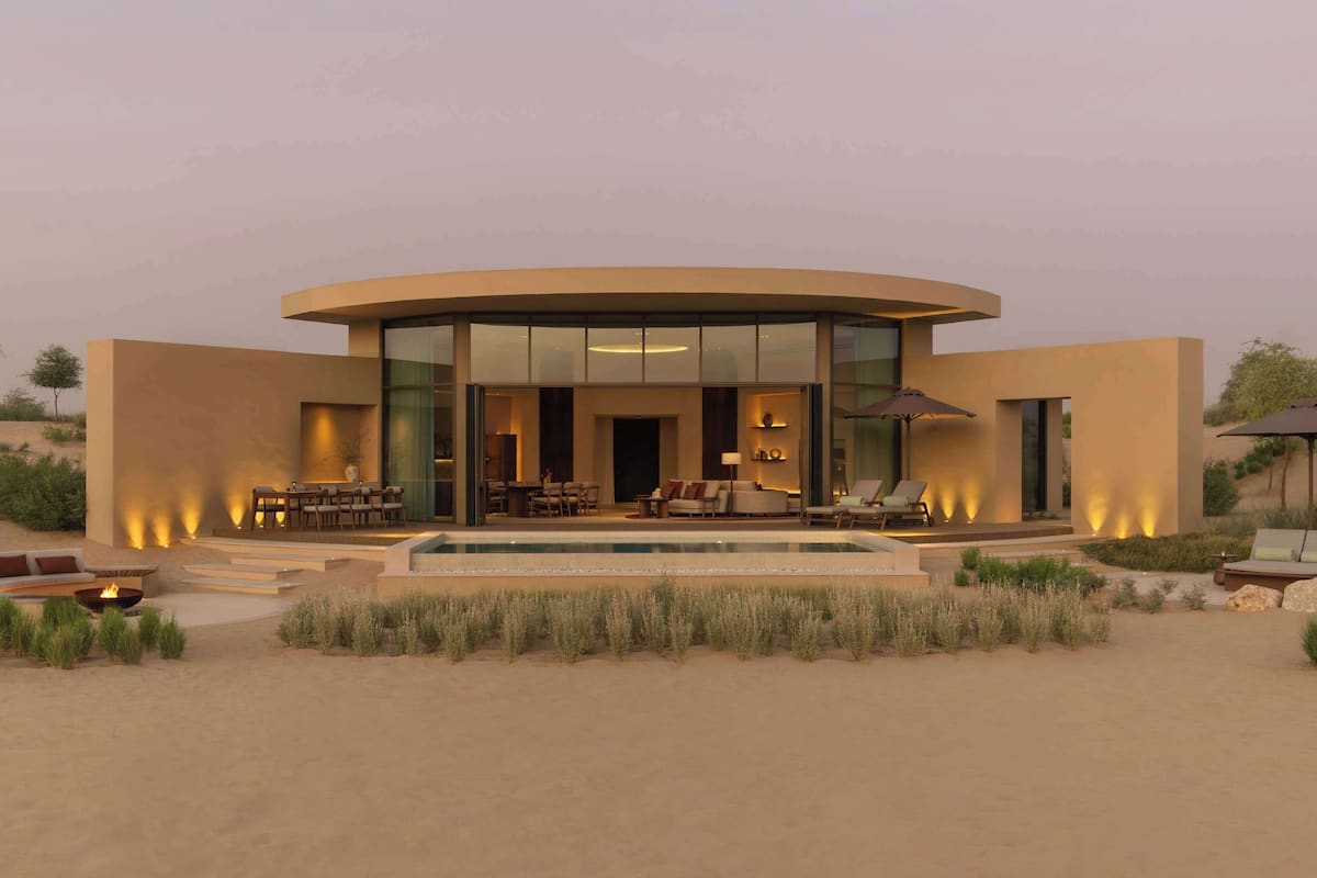 Un edifici modern i circular amb una piscina, zones d'estar a l'exterior i un paisatge desèrtic.