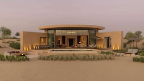 Un edificio moderno y circular con piscina, asientos exteriores y un paisaje desértico.
