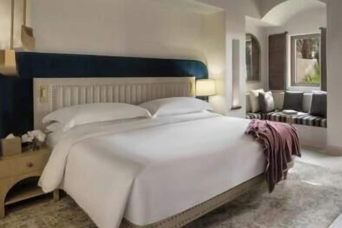 Una cama bien hecha con sábanas blancas, un cabecero azul y una mesita de noche con una lámpara.