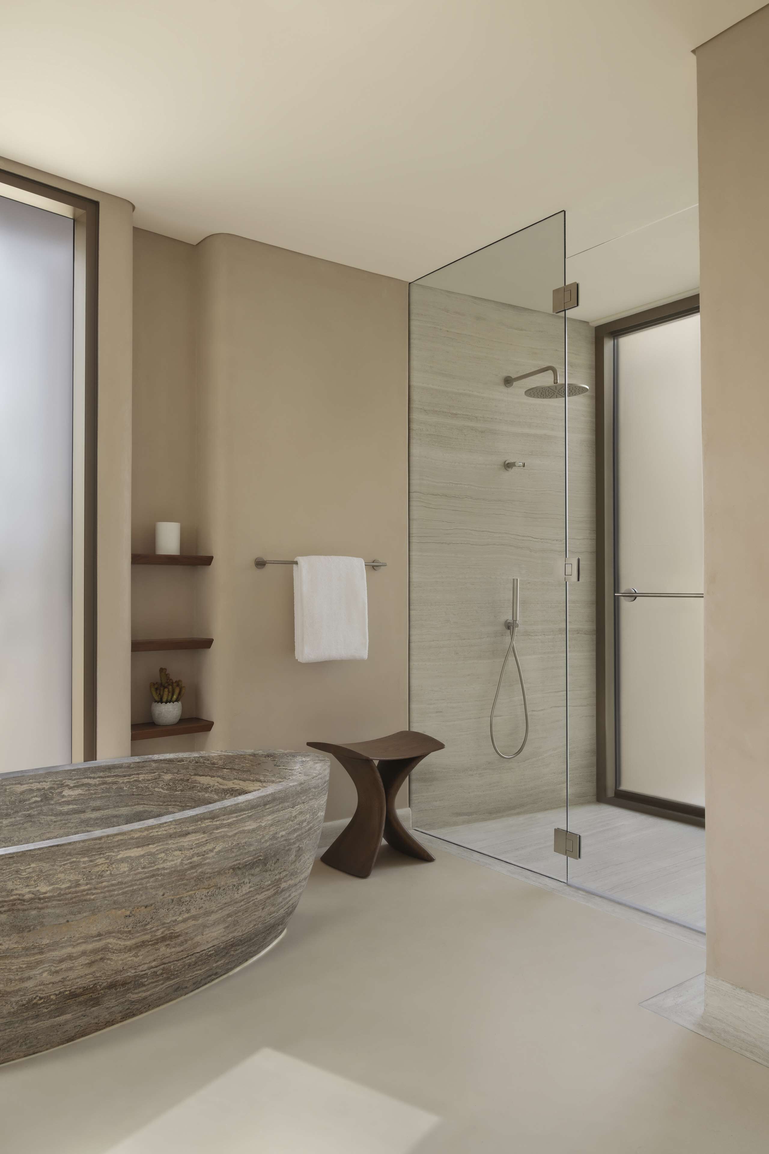 A modern bathroom with a glass shower enclosure, a large stone basin, and minimalist shelving.