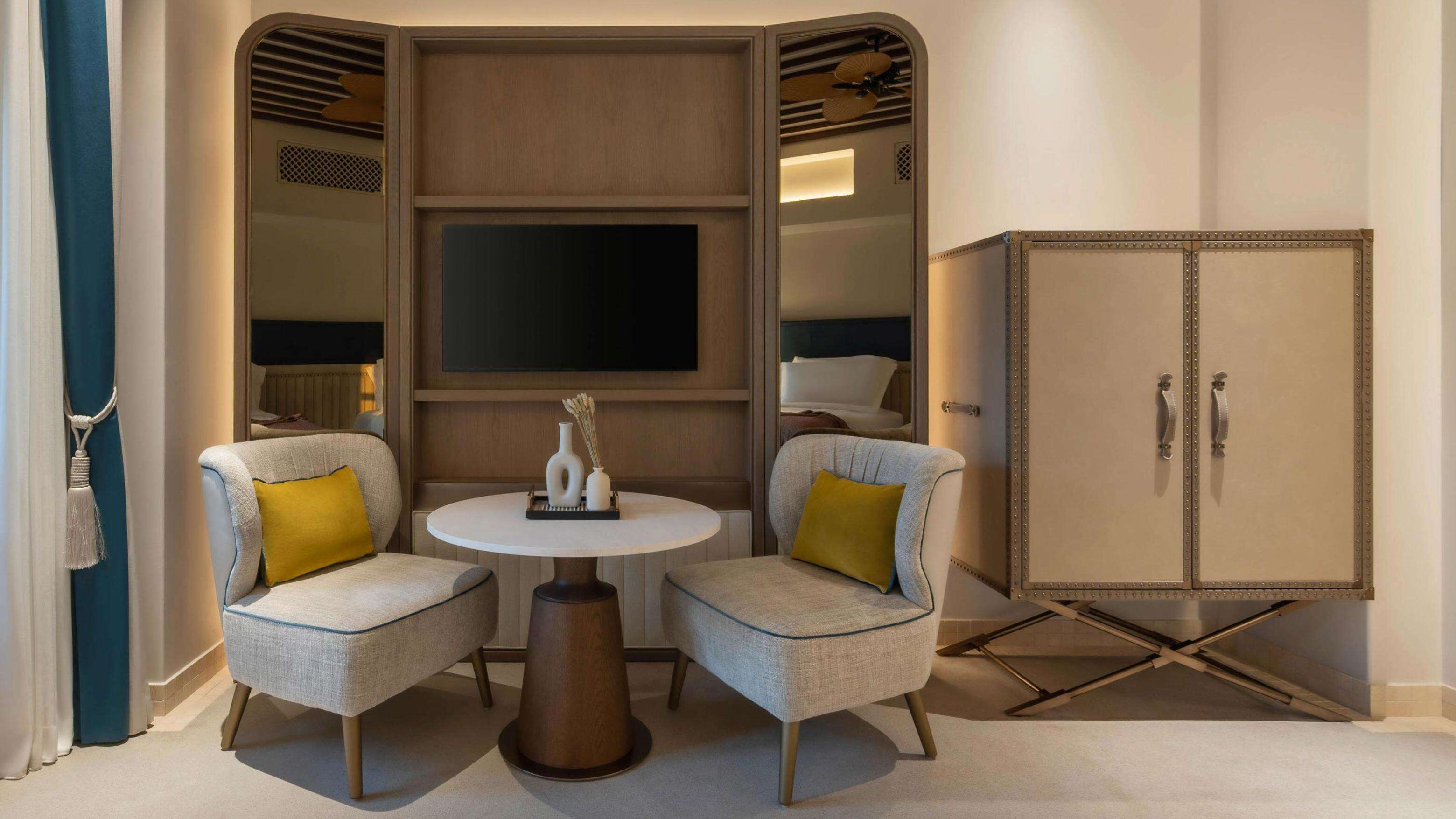 Une chambre moderne comprenant deux fauteuils, une table ronde, un téléviseur à écran plat et un meuble.