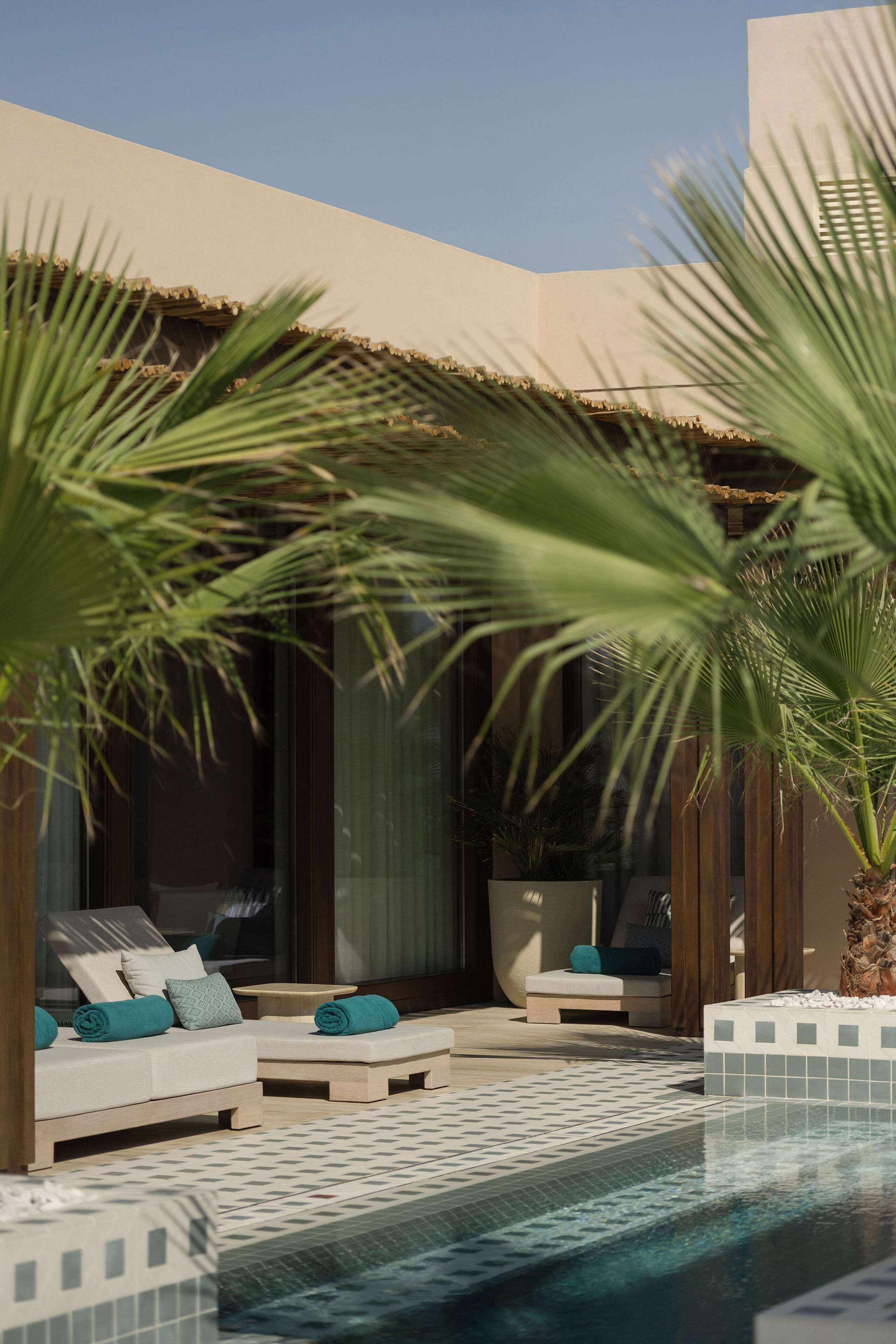 A poolside area with two lounge chairs, a small table, and a palm tree.