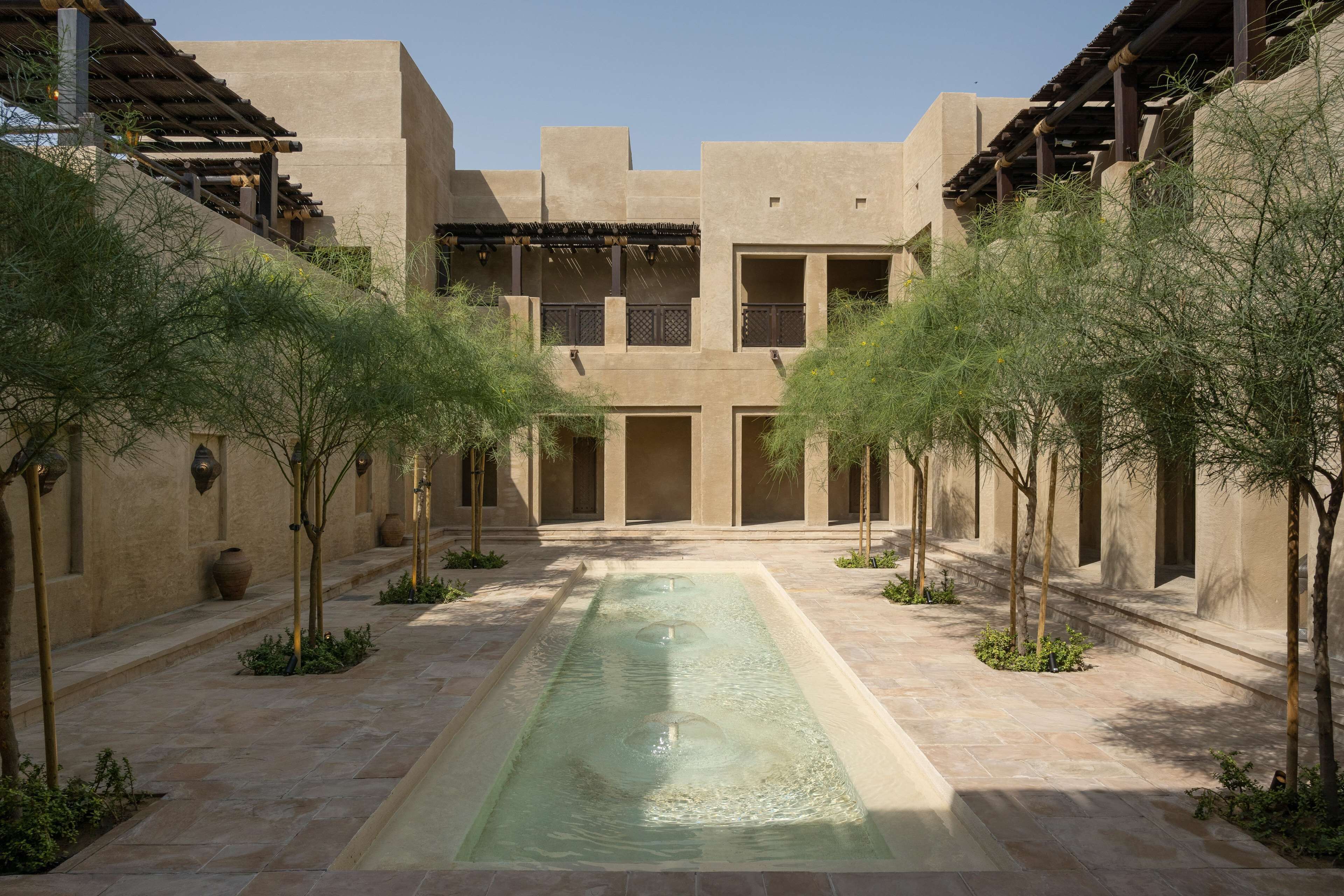 A courtyard with a central water feature, surrounded by low-rise buildings with balconies and a clear sky.