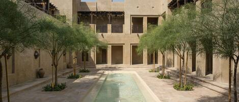 A courtyard with a central water feature, surrounded by low-rise buildings with balconies and a clear sky.