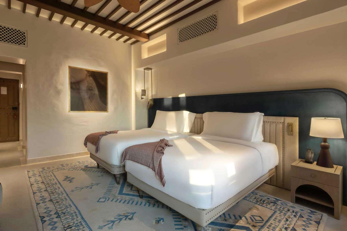 Una habitació d'hotel amb un llit gran, una taula de nit amb una làmpada, una cadira i una catifa amb disseny.