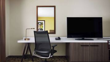 A hotel room with a white desk, a black office chair, a flat-screen TV, and a wooden cabinet.