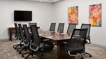 A conference room with a long table, black chairs, a flat-screen TV, and abstract paintings on the walls.