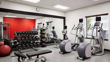 Un gimnasio con diferentes equipos de ejercicio, una banca y una pared roja.