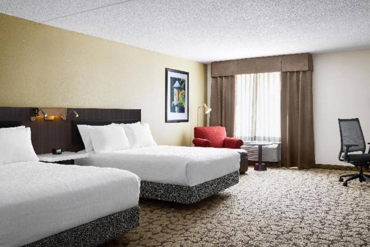 Een hotelkamer met twee bedden, een rode stoel, een bureau en een lamp.