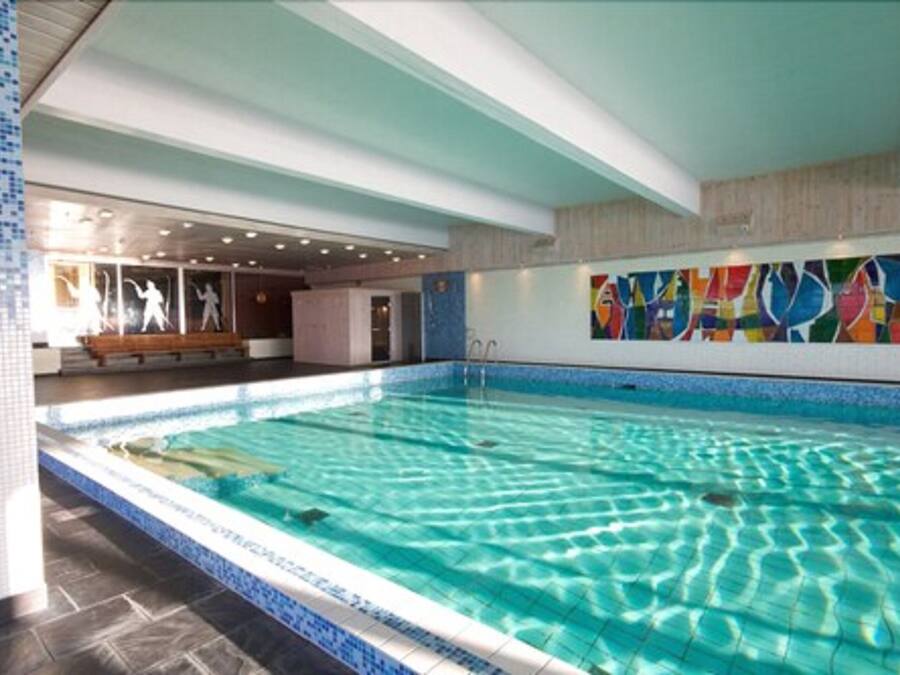 An indoor swimming pool with clear water, tiled walls, and a bench near the entrance.