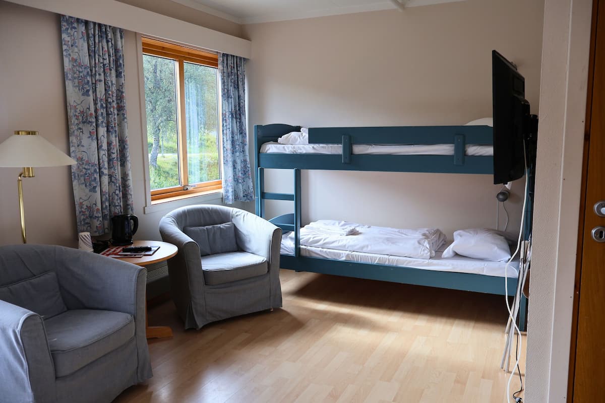 A room with a bunk bed, a desk with a lamp, a chair, and a window with curtains.