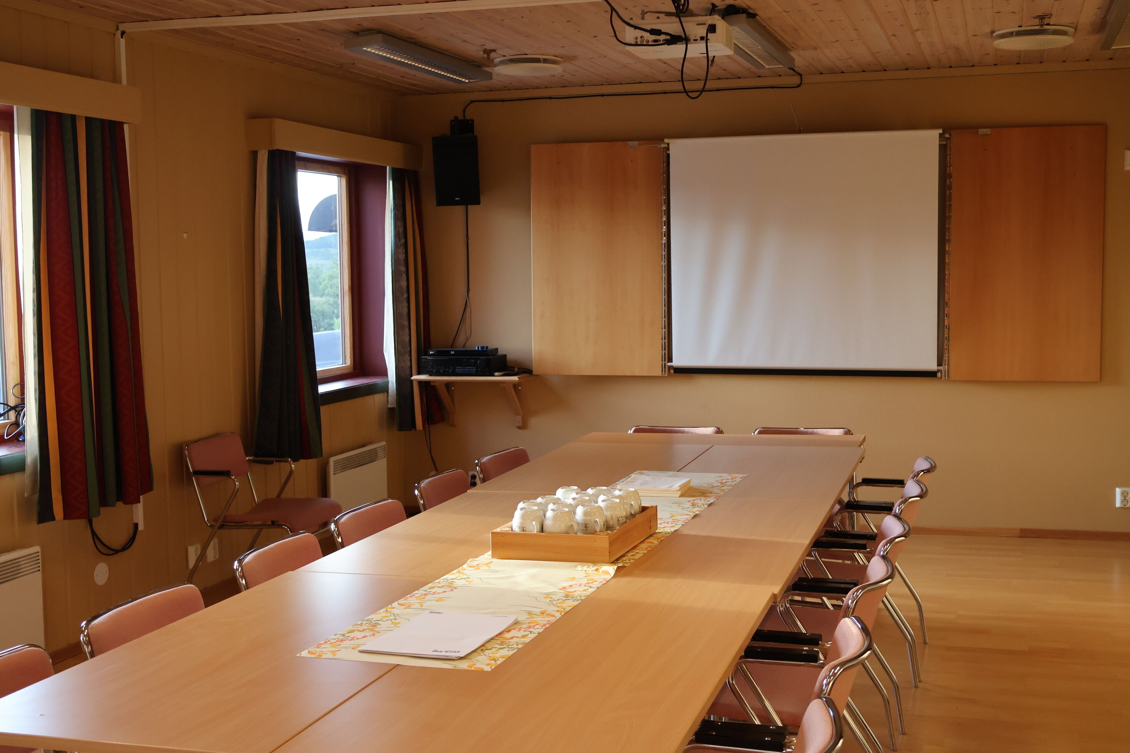 A conference room with a long table, chairs, a projector, and a screen.