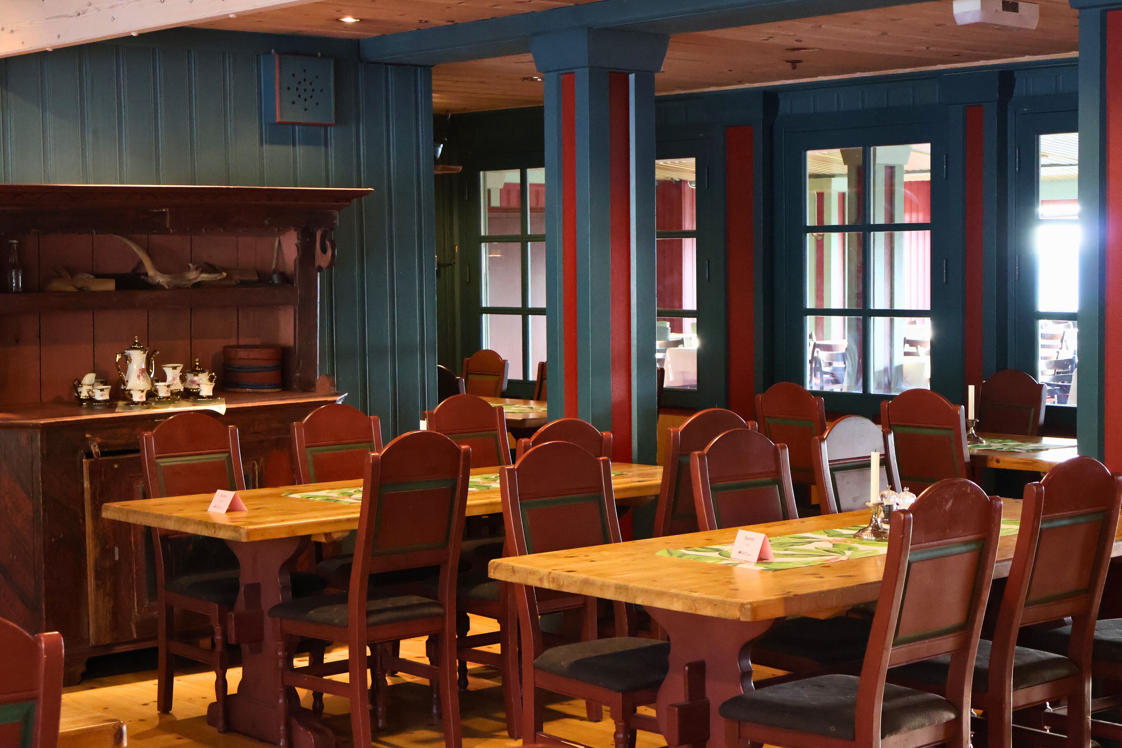 A restaurant with wooden tables and chairs, a bar area with bottles and glasses, and a view of the street through large windows.