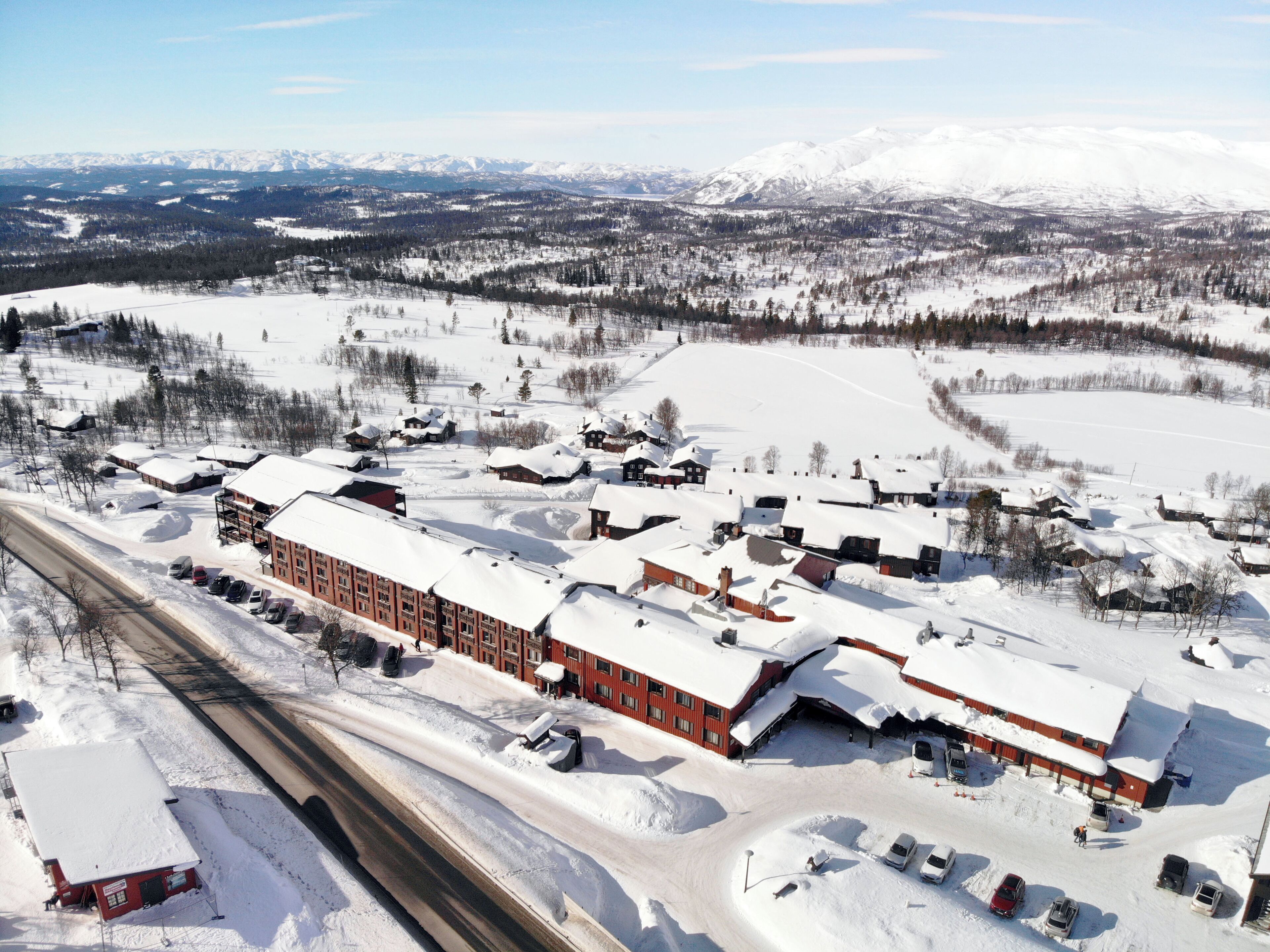 A snow-covered town with a central building complex, surrounded by open fields and distant mountains.