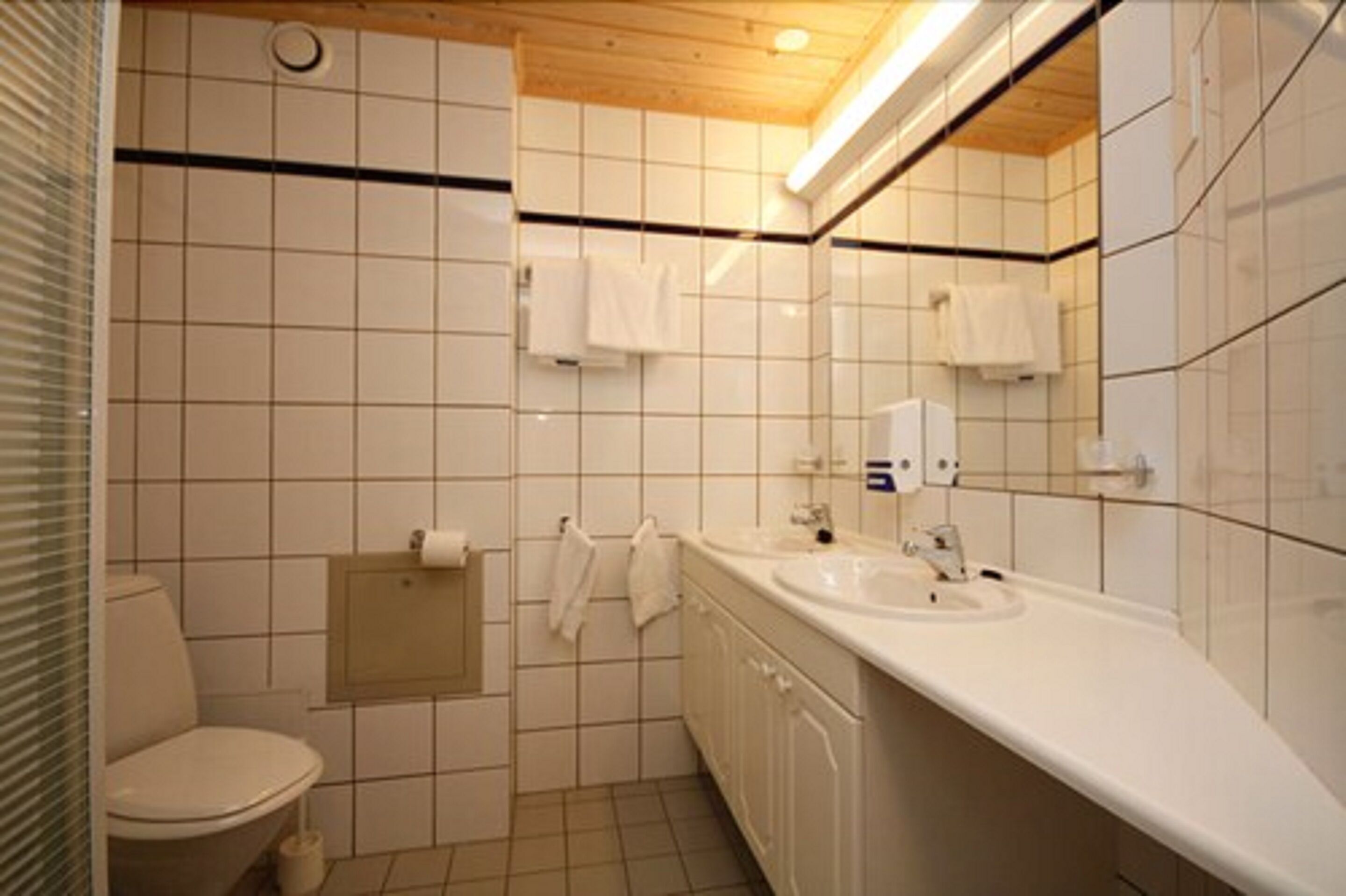 Une petite salle de bain propre, avec des carreaux blancs, des toilettes, un lavabo et un miroir.